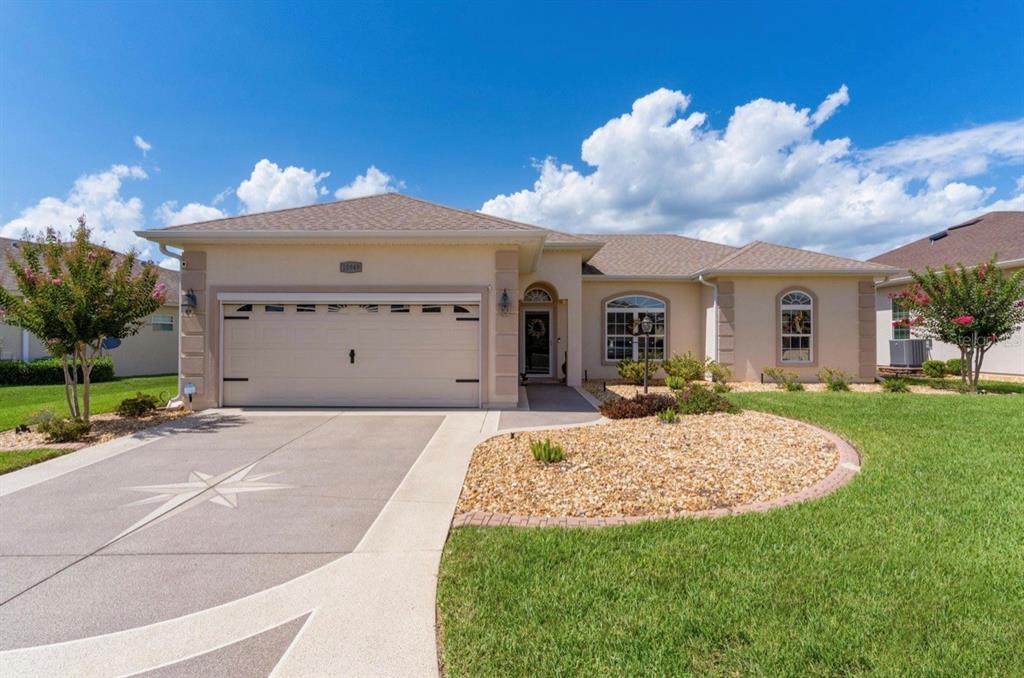 A beige house exterior features a garage, a front entryway, and a gravel garden bed — 10949 SE 169TH LANE, SUMMERFIELD, FL