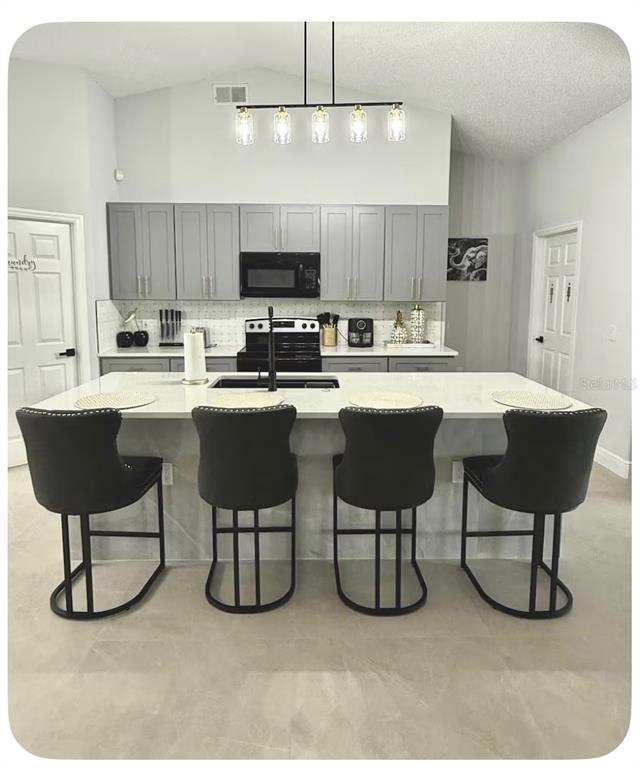 A modern kitchen features gray cabinets, a white island with four stools, and pendant lighting — 80 PUTTER DRIVE, PALM COAST, FL