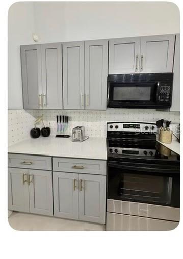 A kitchen features gray cabinets, white countertops, a black microwave, and a black electric stove — 80 PUTTER DRIVE, PALM COAST, FL