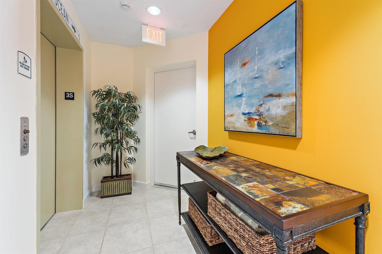 A hallway features a tiled console table, a potted plant, and a painting on a yellow wall — 800 Juno Ocean Walk # 303, Juno Beach FL 33408, JUNO BEACH, FL