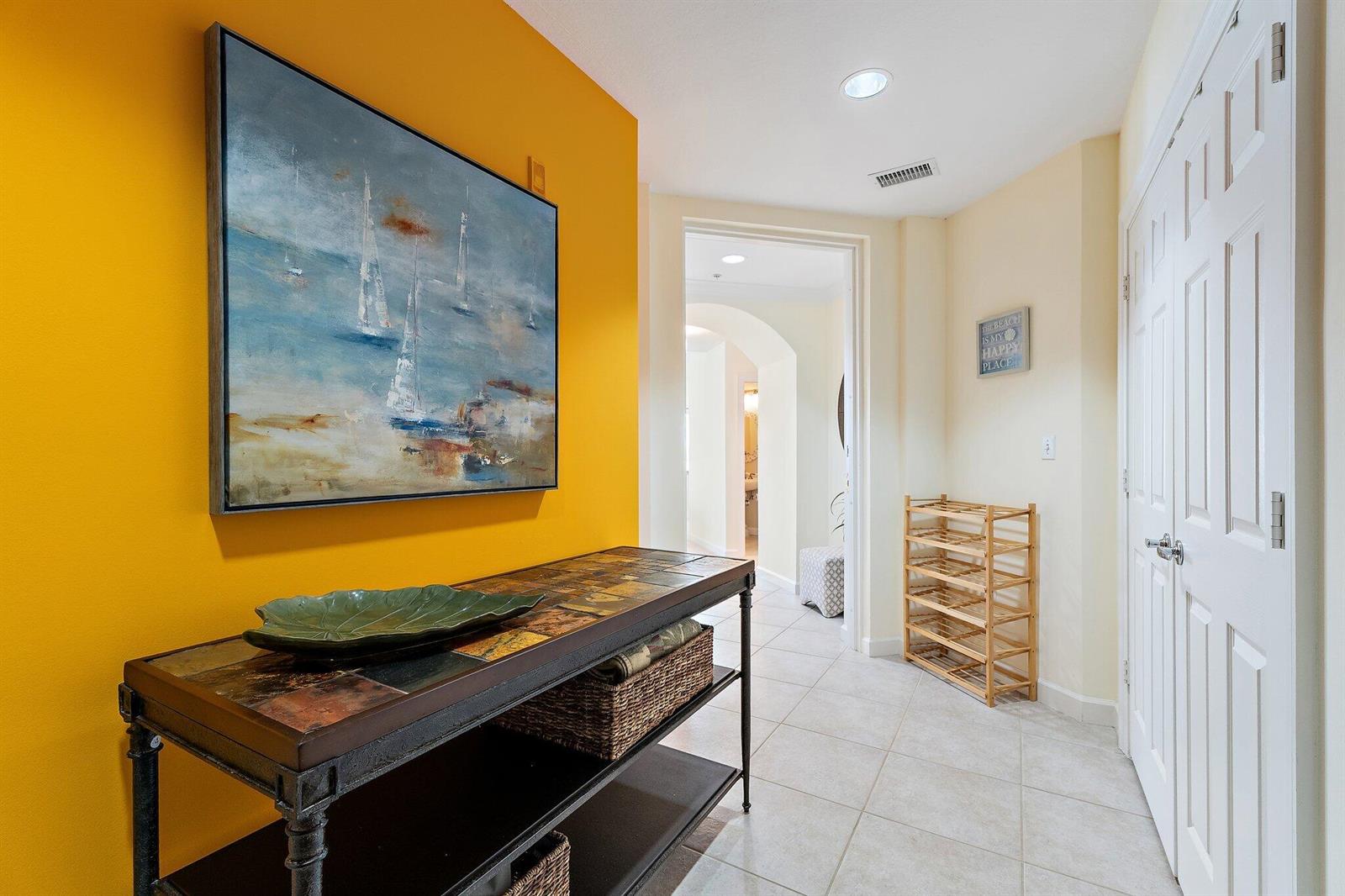 A hallway features a bright yellow accent wall, a console table, and a shoe rack — 800 Juno Ocean Walk # 303, Juno Beach FL 33408, JUNO BEACH, FL