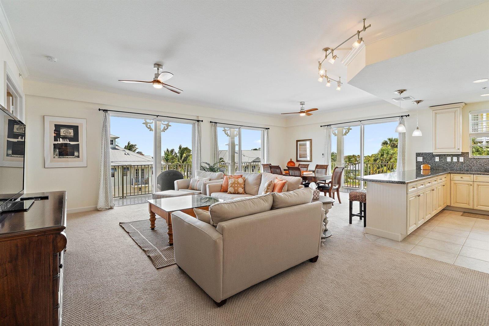 An open-concept living and dining area with carpeted floors, a kitchen island, and balcony access — 800 Juno Ocean Walk # 303, Juno Beach FL 33408, JUNO BEACH, FL