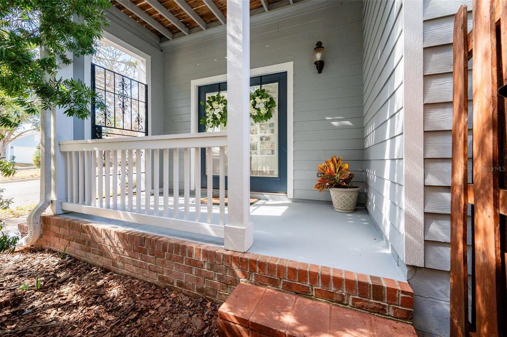 A front porch with a brick base, white railing, and a blue door with wreaths — 11550 NW 17TH PLACE, GAINESVILLE, FL
