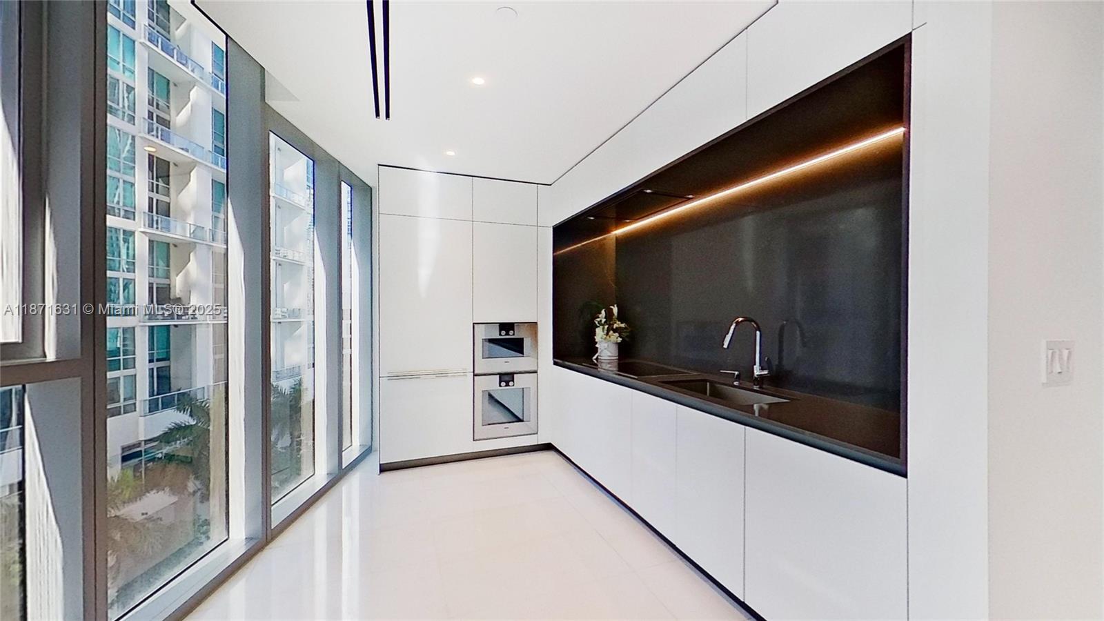 A modern kitchen features white cabinetry, dark countertops, built-in appliances, and floor-to-ceiling windows — 300 Biscayne Blvd Way # 506E, Miami FL 33131, MIAMI, FL