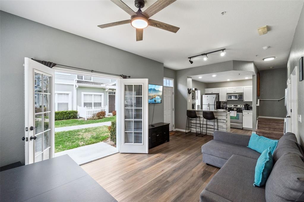 An open-concept living room and kitchen featuring wood-look flooring, a ceiling fan, and French doors — 2215 SAN VITTORINO CIRCLE UNIT 102, KISSIMMEE, FL