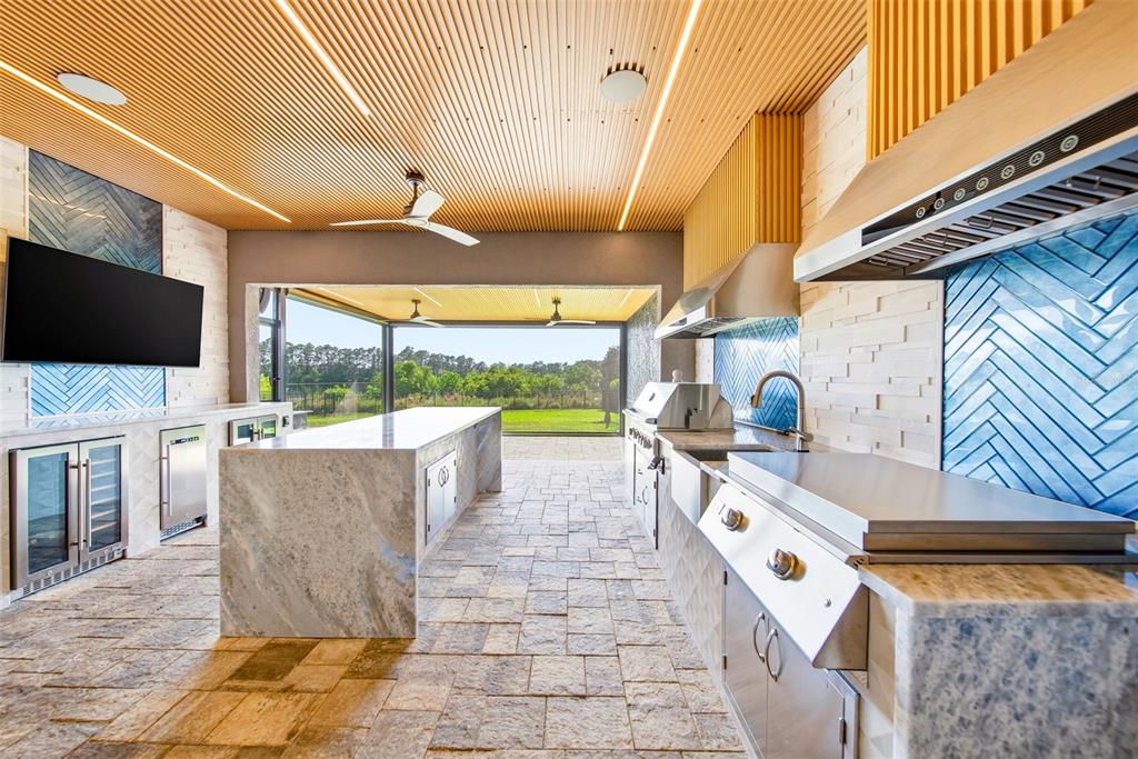 An outdoor kitchen features stone countertops, blue herringbone tile backsplashes, and a slatted wood ceiling — 10174 MERRYMEETING BAY DRIVE, WINTER GARDEN, FL