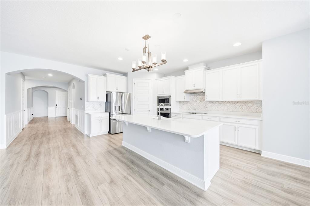 A modern kitchen features white cabinetry, a central island, and light wood-look flooring — 10174 MERRYMEETING BAY DRIVE, WINTER GARDEN, FL