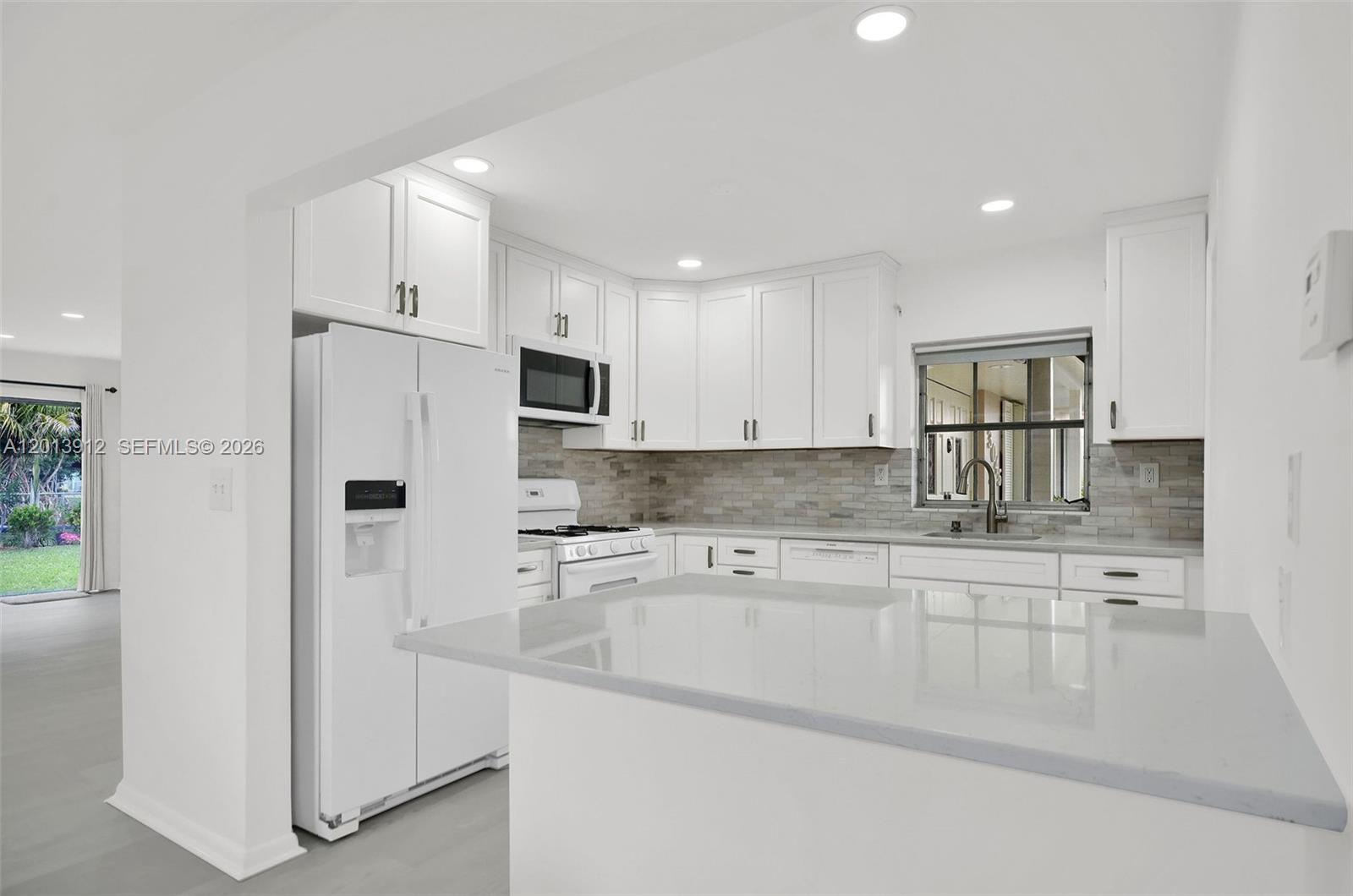 A white kitchen features a quartz countertop island, white cabinetry, and a subway tile backsplash — 3045 SW 124th Ct, Miami FL 33175, MIAMI, FL