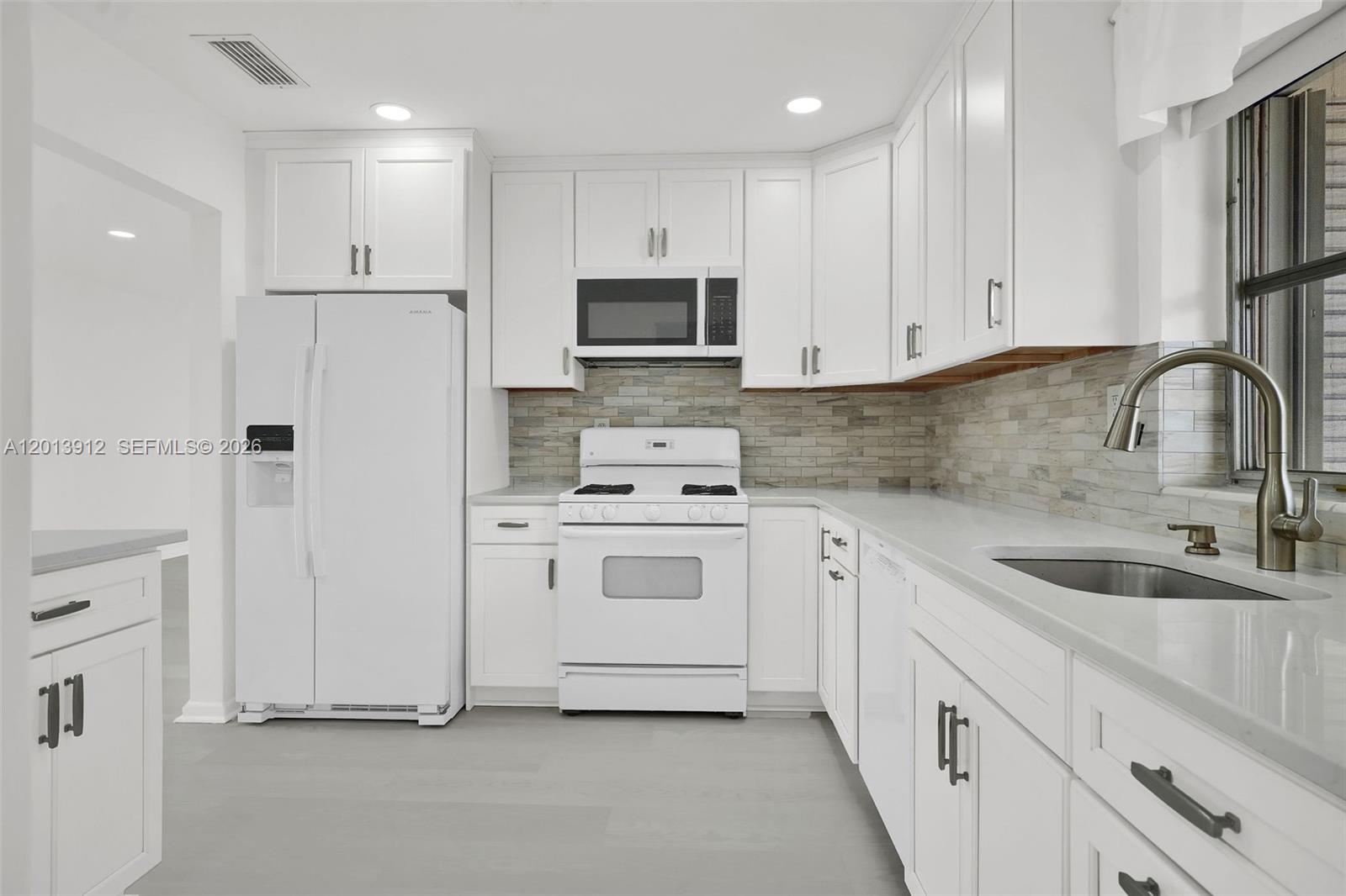 A white kitchen features white cabinetry, stainless steel hardware, and a stone tile backsplash — 3045 SW 124th Ct, Miami FL 33175, MIAMI, FL