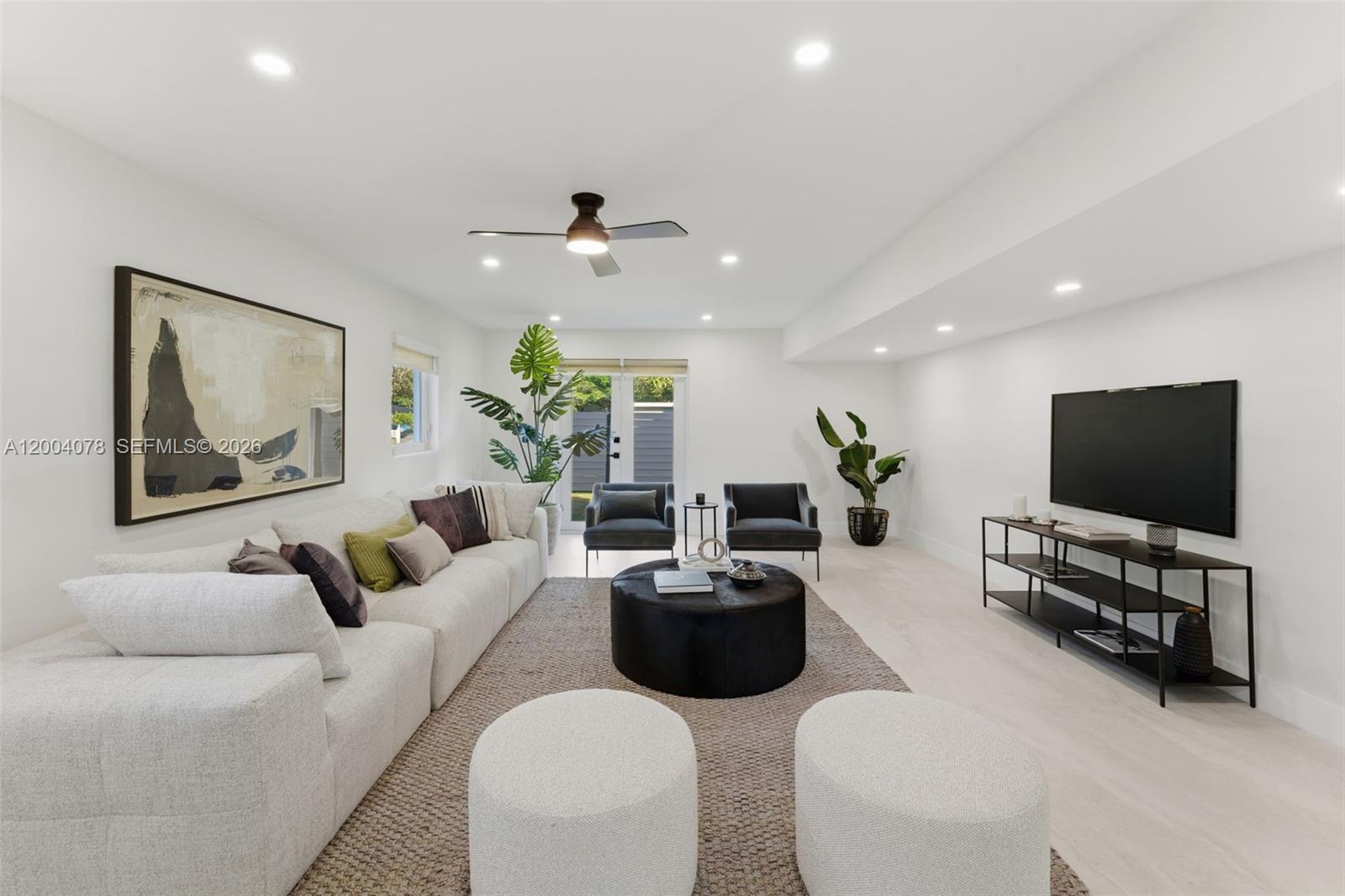 A modern living room features a white sectional sofa, black circular ottoman, and television console — 13225 SW 83rd Ct, Pinecrest FL 33156, PINECREST, FL