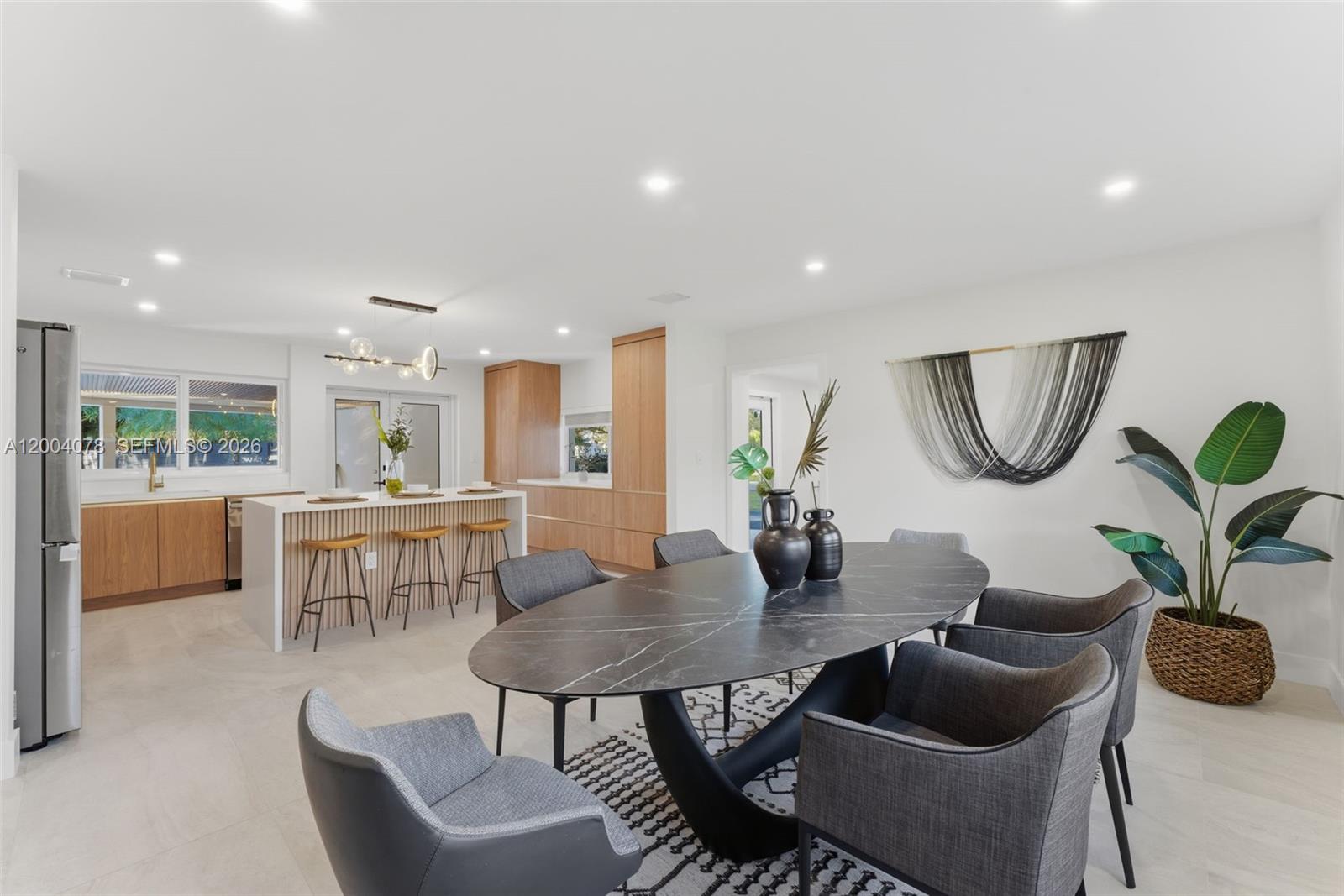 A modern dining area features an oval marble table, grey chairs, and an open kitchen — 13225 SW 83rd Ct, Pinecrest FL 33156, PINECREST, FL