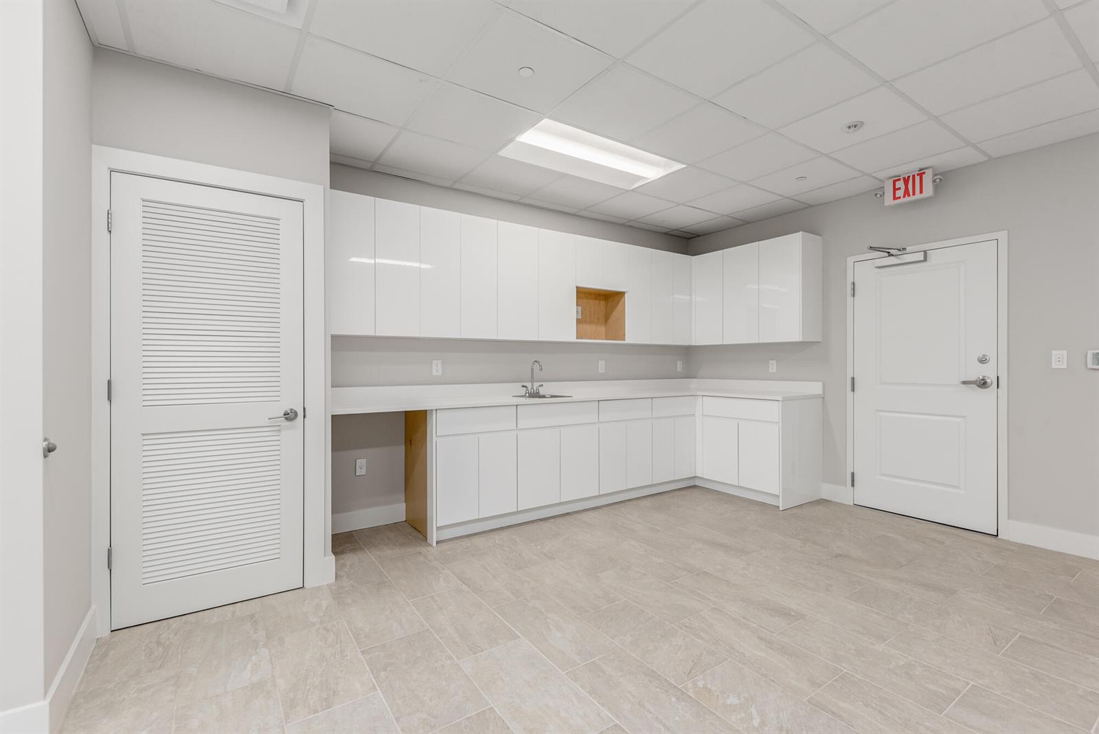 A breakroom features white cabinets, a sink, light-colored tile flooring, and two white doors — 41 SW Seminole Street # 210, Stuart FL 34994, STUART, FL