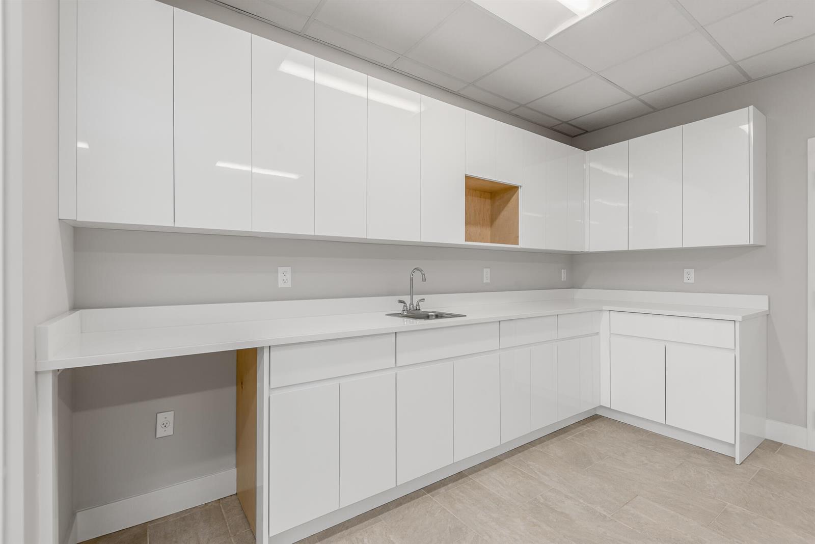 A modern kitchen or breakroom features white glossy cabinetry, a sink, and light-colored countertops — 41 SW Seminole Street # 210, Stuart FL 34994, STUART, FL