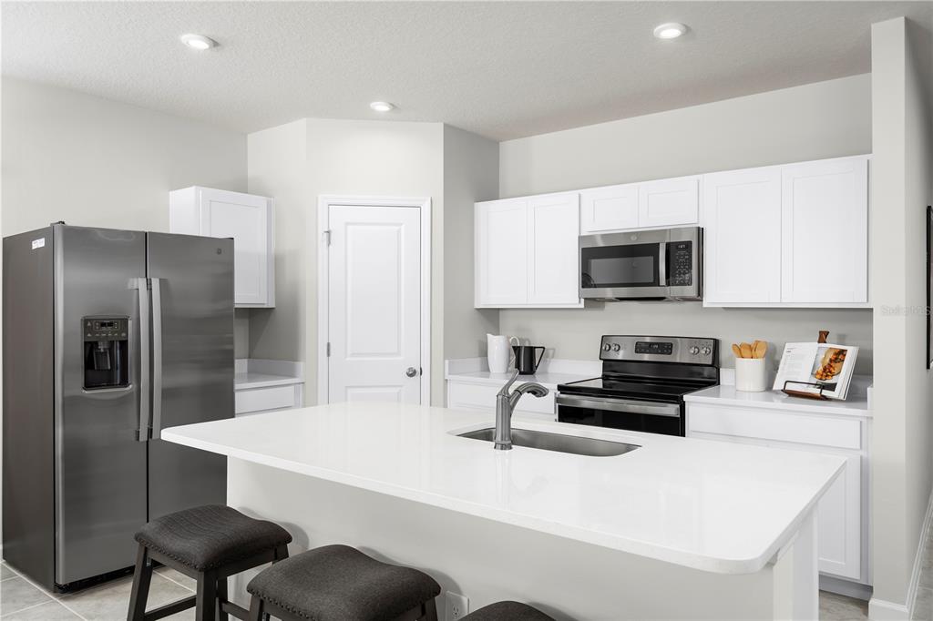 A kitchen features white cabinets, stainless steel appliances, a center island, and dark bar stools — 1111 HICKORY BRANCH DRIVE, LAKELAND, FL