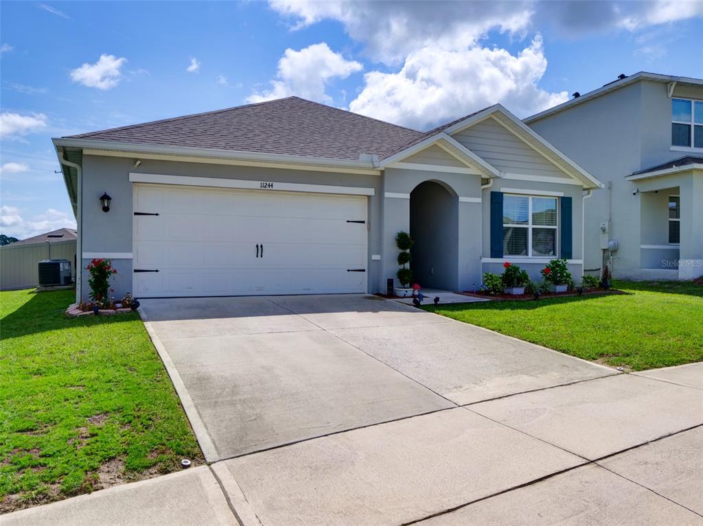 A single-story house with a gray stucco exterior, a two-car garage, and a concrete driveway — 11244 AMBER RIDGE DRIVE, ZELLWOOD, FL