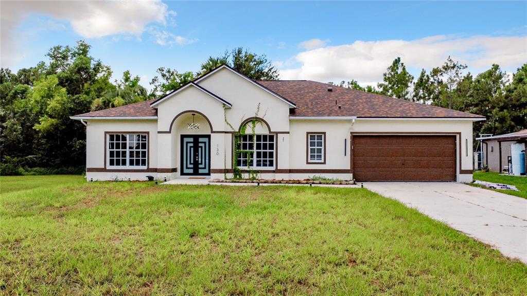 A single-story house with a stucco exterior, brown roof, and a two-car garage — 130 16TH AVENUE NE, NAPLES, FL