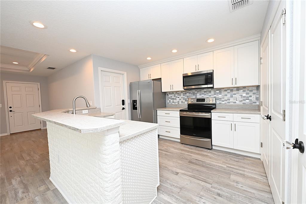 A kitchen features white cabinets, stainless steel appliances, a brick-faced island, and light wood flooring — 5662 TOWER PALMS LANE, LAKELAND, FL