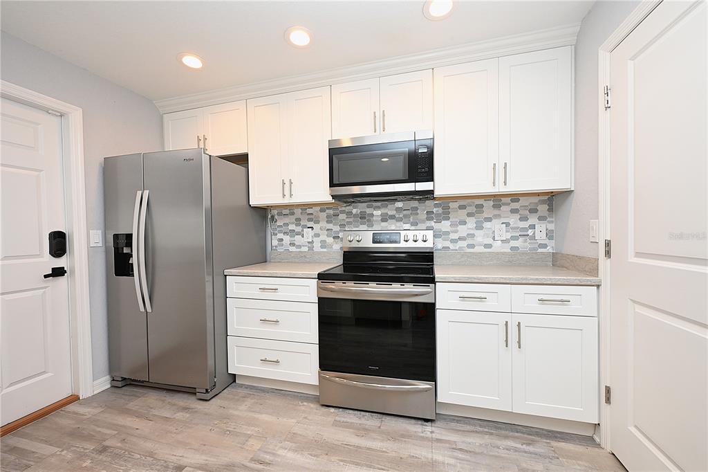 A kitchen features white cabinets, stainless steel appliances, and a gray patterned tile backsplash — 5662 TOWER PALMS LANE, LAKELAND, FL