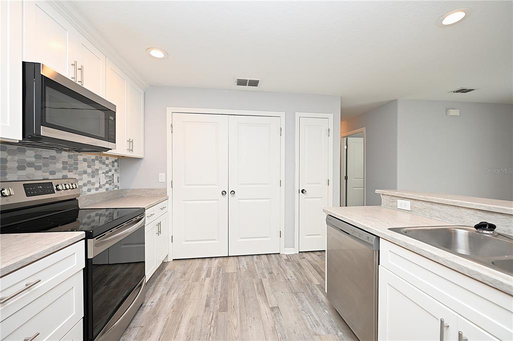 A kitchen features white cabinets, stainless steel appliances, a tiled backsplash, and light wood flooring — 5662 TOWER PALMS LANE, LAKELAND, FL