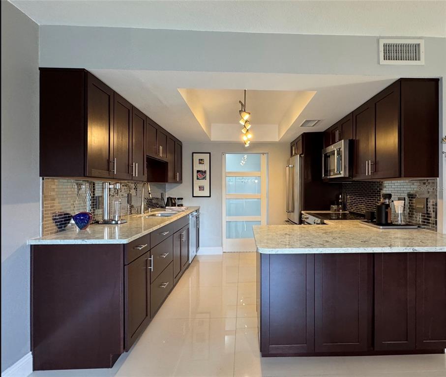 A kitchen features dark wood cabinets, light granite countertops, a tiled backsplash, and tile flooring — 108 MADRID DRIVE UNIT D, CASSELBERRY, FL