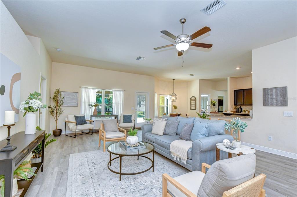 A bright living room features light wood flooring, a blue sofa, and a ceiling fan — 3358 PONYTAIL COURT, SPRING HILL, FL