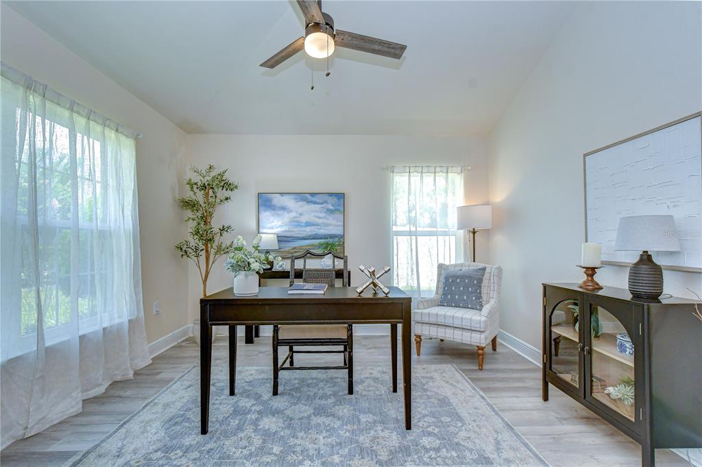 A home office features a dark wood desk, a patterned armchair, and light wood flooring — 3358 PONYTAIL COURT, SPRING HILL, FL