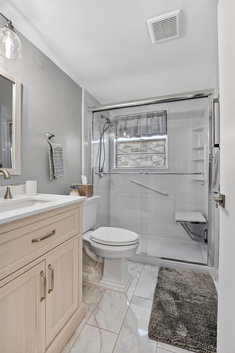 A bathroom features a light wood vanity, a white toilet, and a glass-enclosed walk-in shower — 150 Mansfield D # 150, Boca Raton FL 33434, BOCA RATON, FL