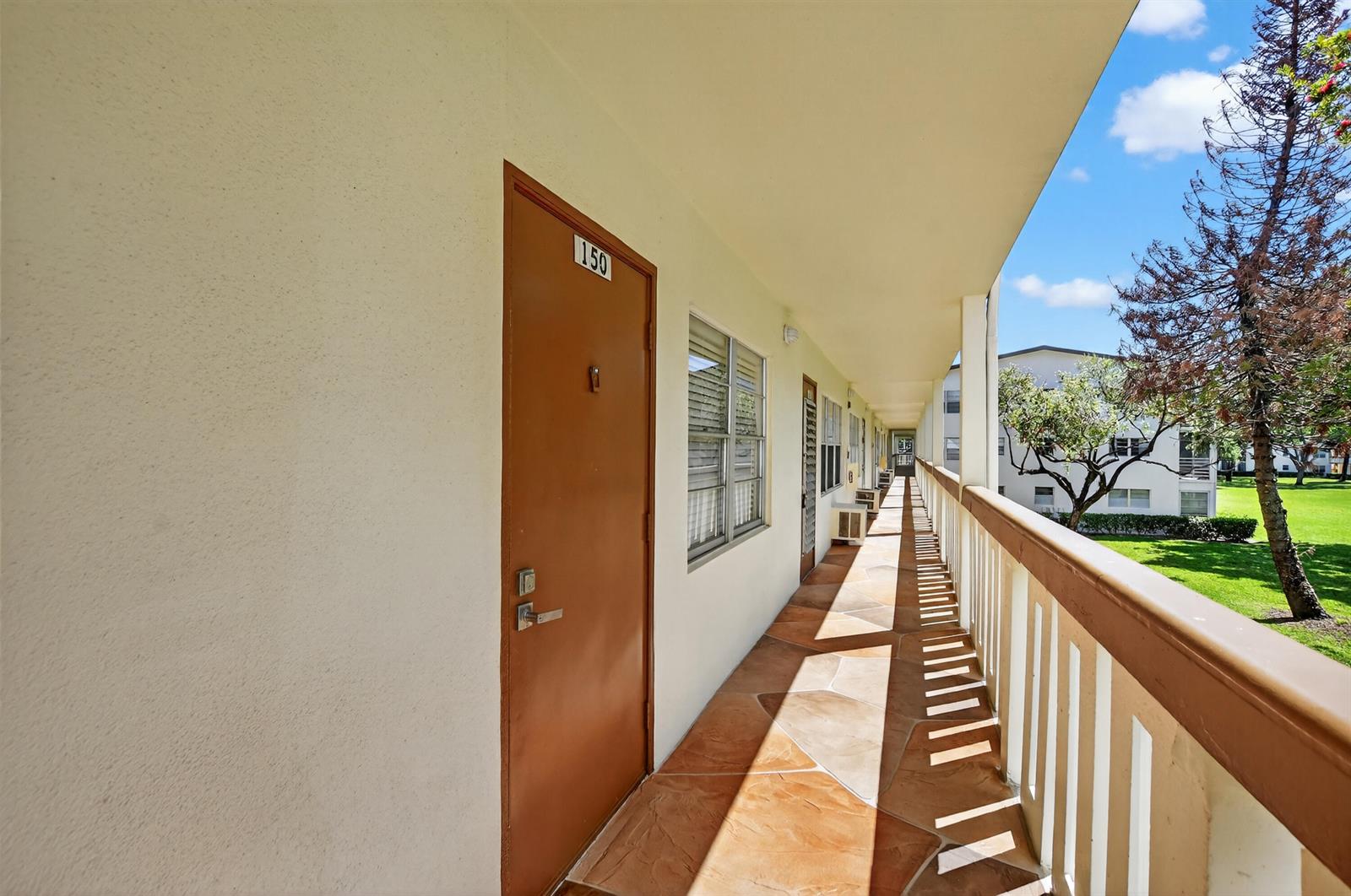 An outdoor apartment building walkway with a brown door labeled 150 and tiled flooring — 150 Mansfield D # 150, Boca Raton FL 33434, BOCA RATON, FL