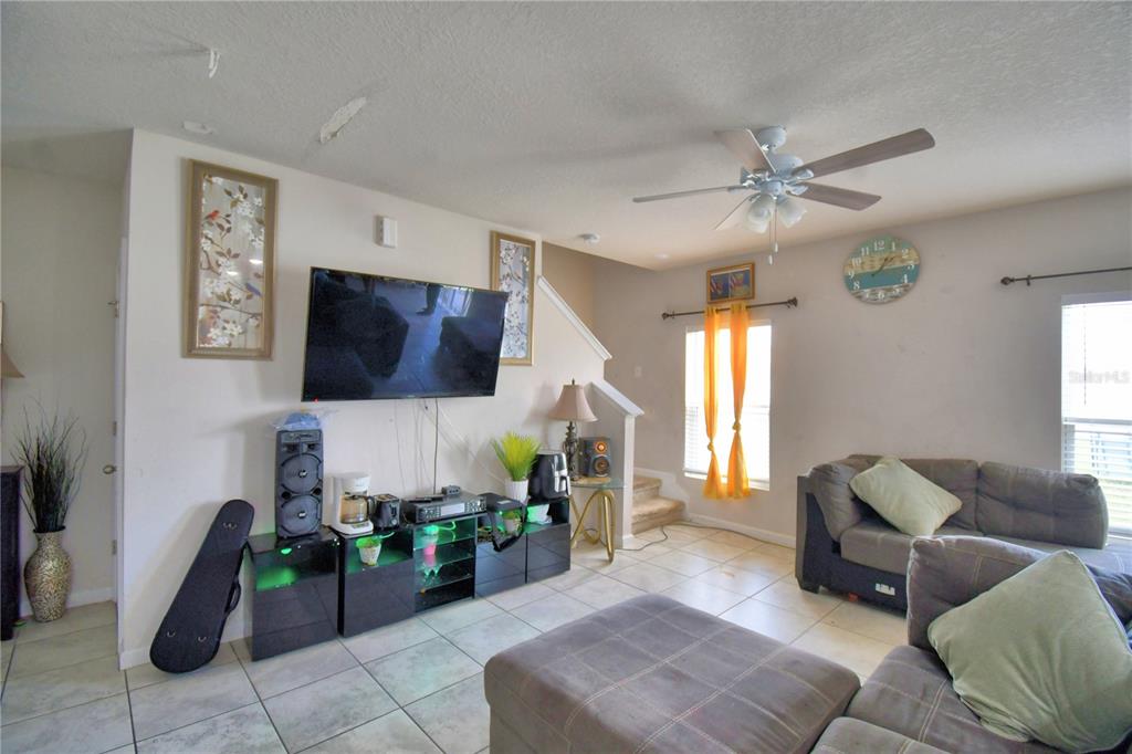 A living room features a wall-mounted television, a media console, tile flooring, and a sofa — 1533 MAJESTIC LANE, WINTER HAVEN, FL