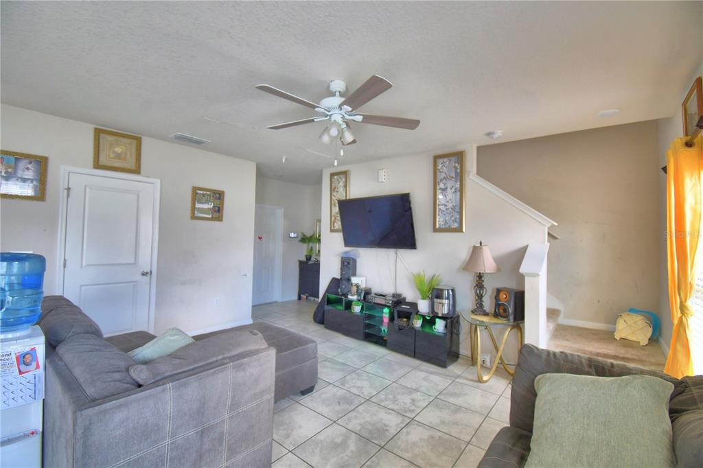 A living room features a gray sectional sofa, a wall-mounted television, and tile flooring — 1533 MAJESTIC LANE, WINTER HAVEN, FL