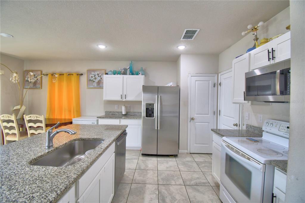 A kitchen features white cabinets, granite countertops, stainless steel appliances, and tile flooring — 1533 MAJESTIC LANE, WINTER HAVEN, FL