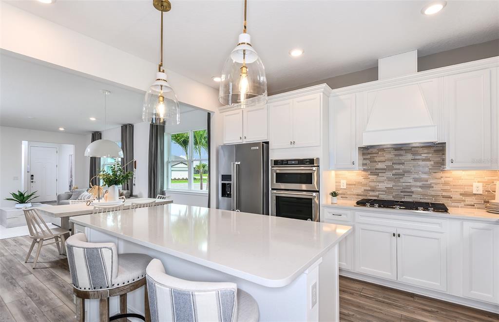 A modern kitchen features white cabinetry, a large quartz island, and stainless steel appliances — 5450 SW 86TH COURT ROAD, OCALA, FL