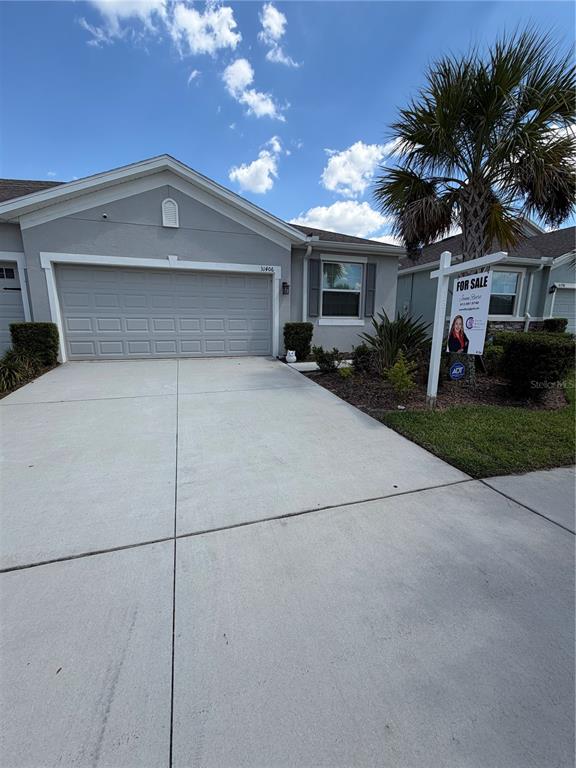 A gray single-story house features a two-car garage, a concrete driveway, and a for-sale sign — 31406 MANGO FADE WAY, SAN ANTONIO, FL
