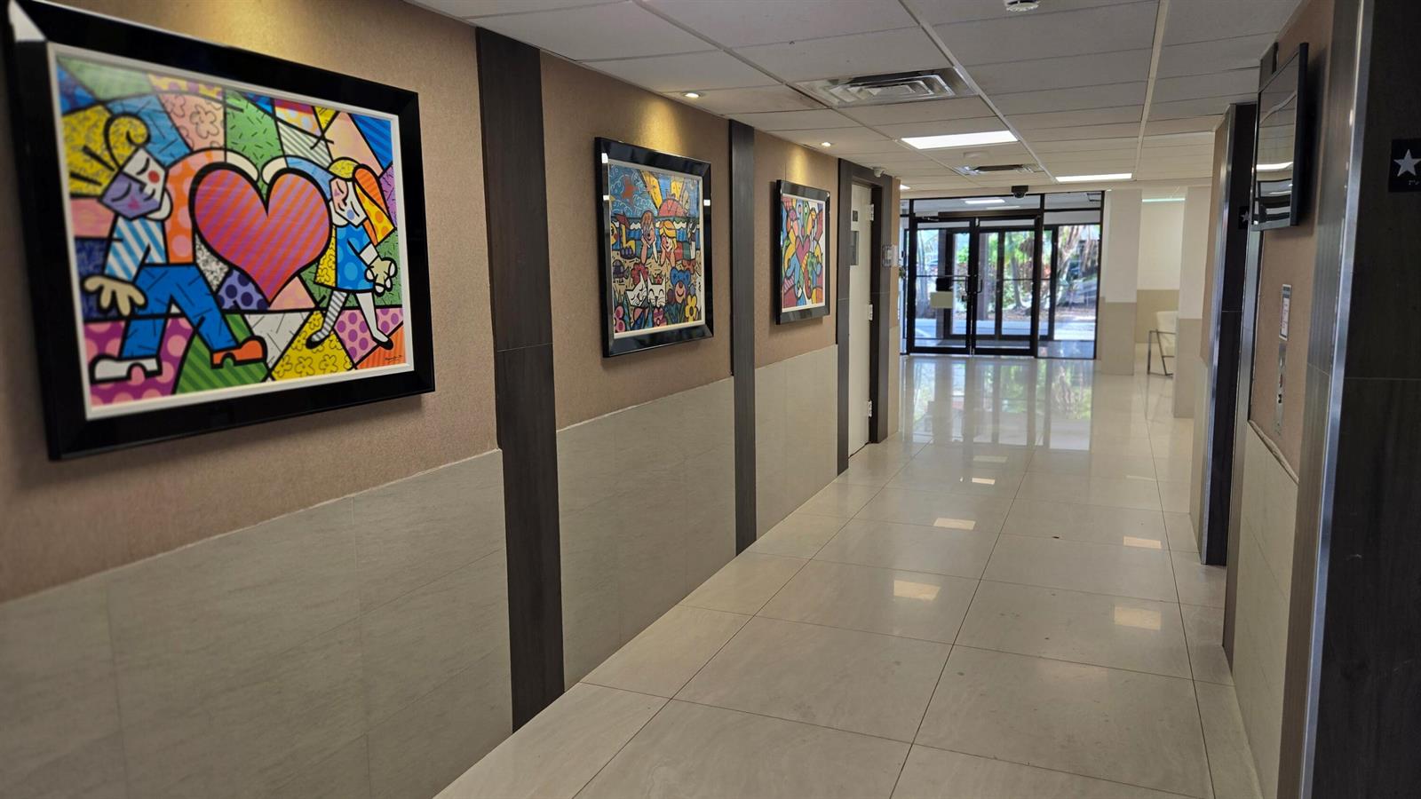A brightly lit hallway features tiled floors, dark wood accents, and colorful framed artwork — 4164 Inverrary Drive # 601, Lauderhill FL 33319, LAUDERHILL, FL