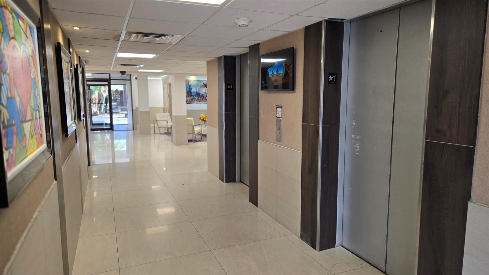 A hallway features two silver elevators, tiled floors, and framed artwork on the walls — 4164 Inverrary Drive # 601, Lauderhill FL 33319, LAUDERHILL, FL