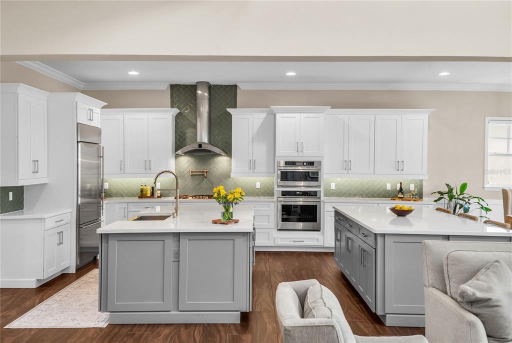 A modern kitchen features white cabinetry, gray islands, stainless steel appliances, and a green backsplash — 12521 FARADAY LANE, ORLANDO, FL