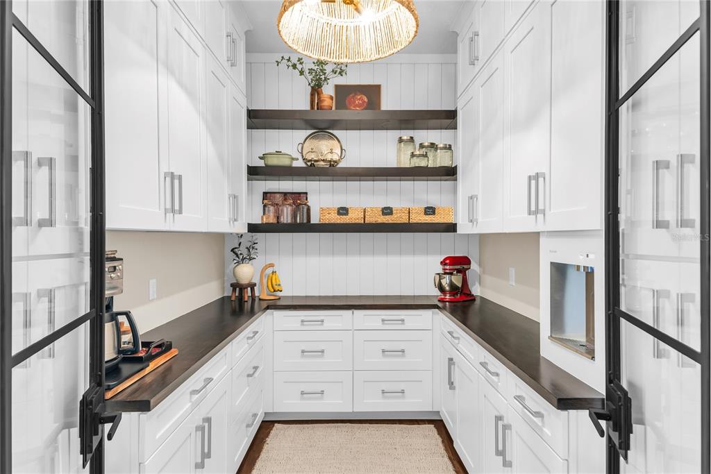 A walk-in pantry features white cabinetry, dark wood countertops, open shelving, and glass-paned doors — 12521 FARADAY LANE, ORLANDO, FL