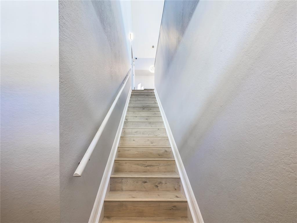 A straight staircase with light wood-look treads and a white handrail ascends between gray walls — 5521 ROSEHILL ROAD UNIT 203, SARASOTA, FL