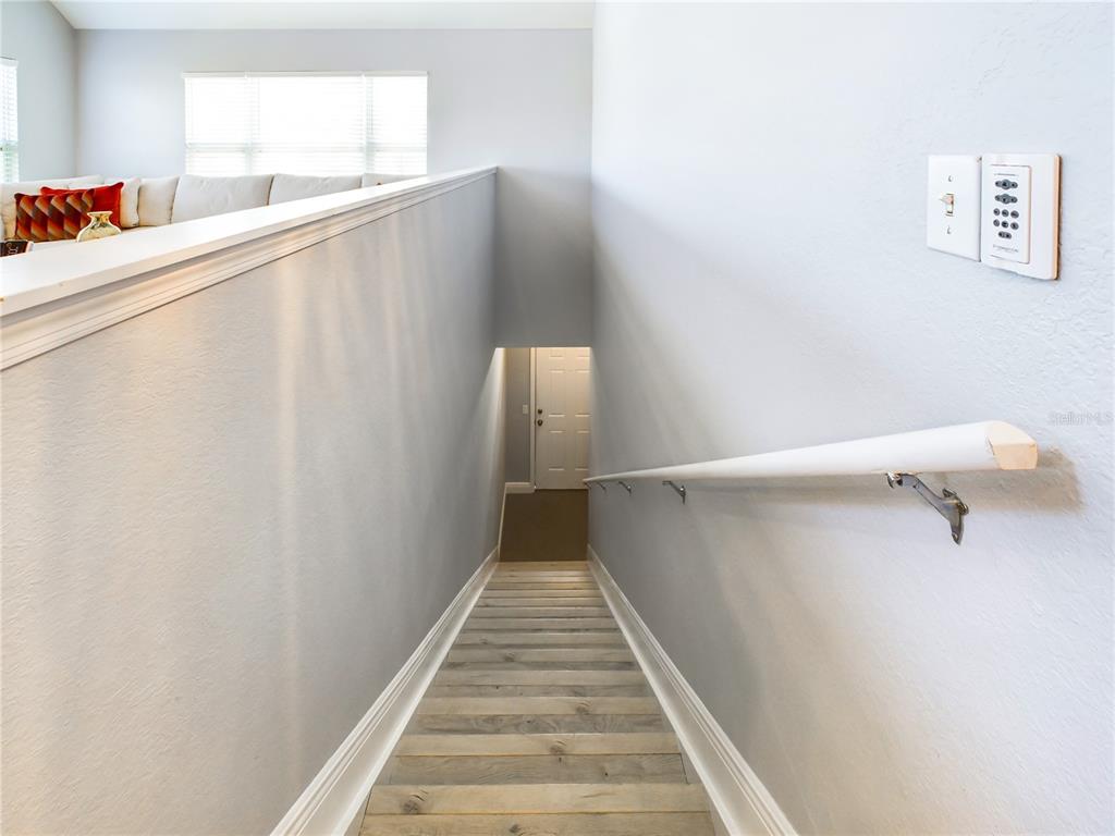 A staircase with wood-look steps leads down to a white door in a hallway — 5521 ROSEHILL ROAD UNIT 203, SARASOTA, FL
