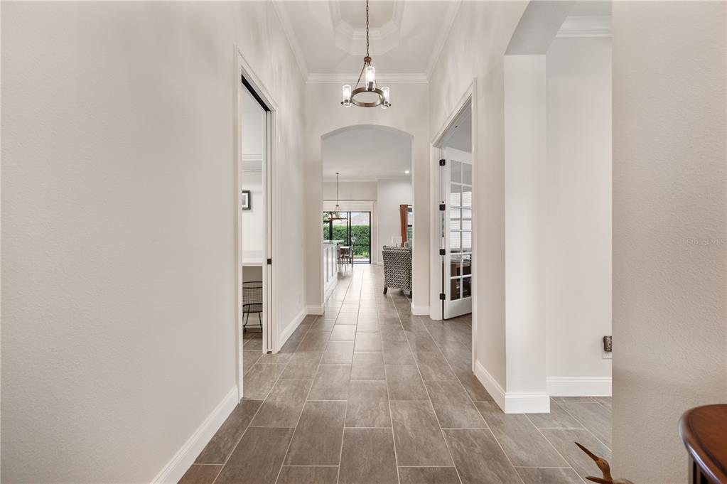 A hallway with gray tile flooring leads toward a bright living area with glass doors — 7783 LAKE JAMES BOULEVARD, LAKELAND, FL