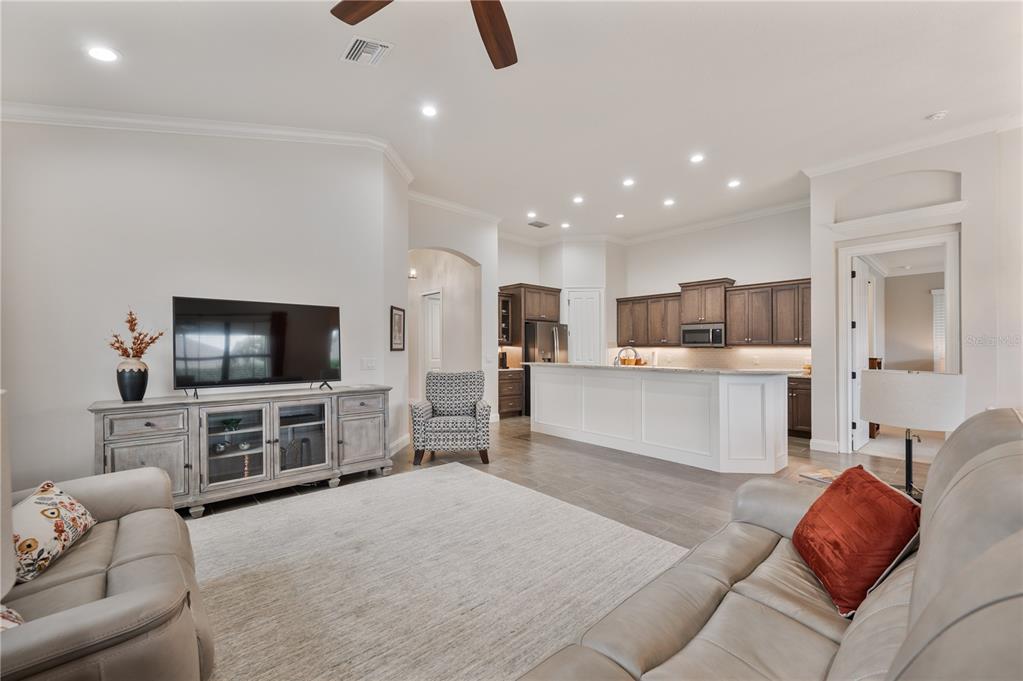 A living room with a television console, gray sofas, and an open kitchen with island — 7783 LAKE JAMES BOULEVARD, LAKELAND, FL