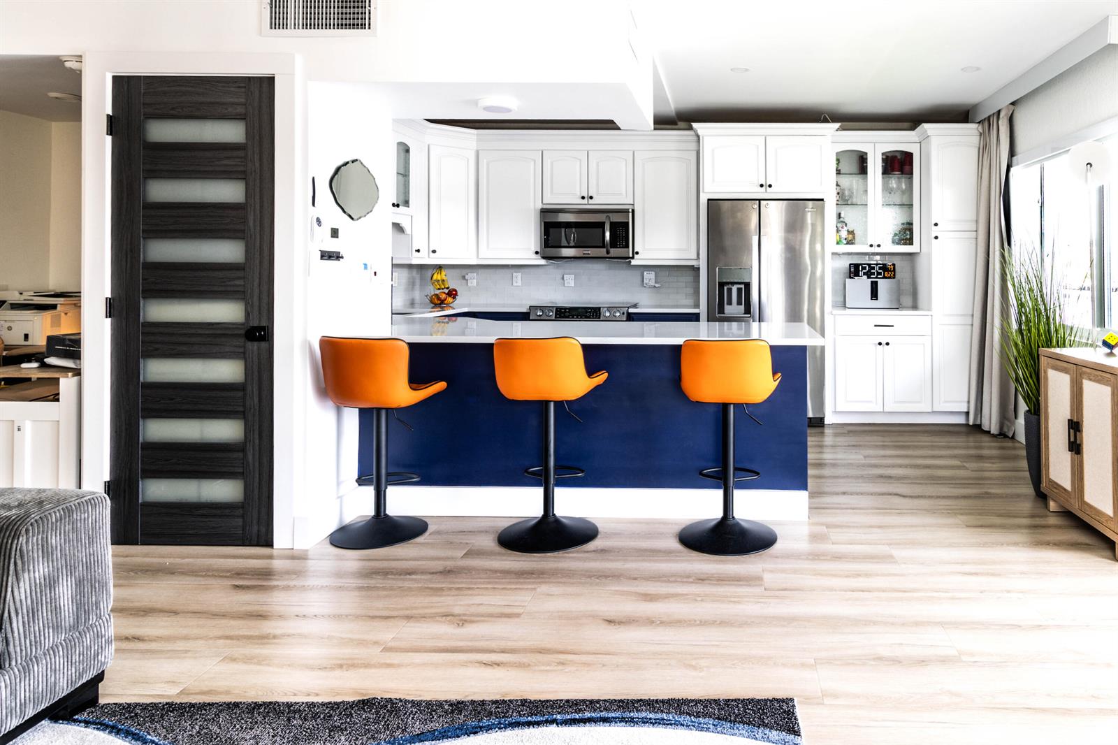 A kitchen features a blue island with three orange bar stools and white cabinetry — 1201 S Riverside Drive # 208, Pompano Beach FL 33062, POMPANO BEACH, FL