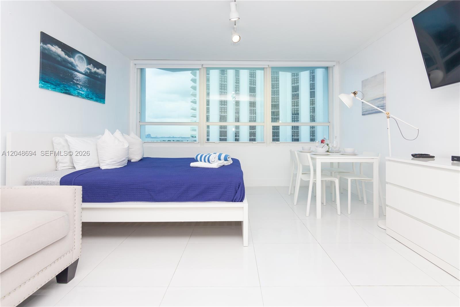 A bright studio apartment features a bed, dining area, and large windows with city views — 5445 Collins Ave # 908, Miami Beach FL 33140, MIAMI BEACH, FL