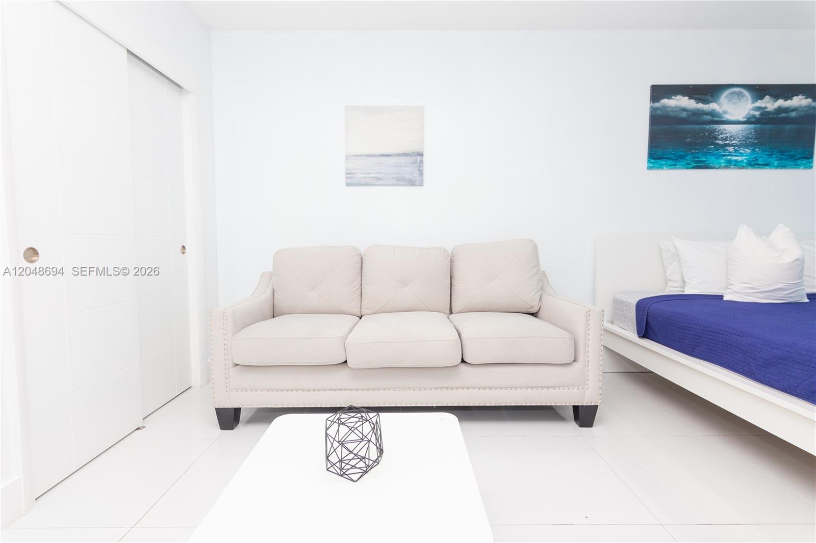 A white room features a beige sofa, a white coffee table, and a bed — 5445 Collins Ave # 908, Miami Beach FL 33140, MIAMI BEACH, FL