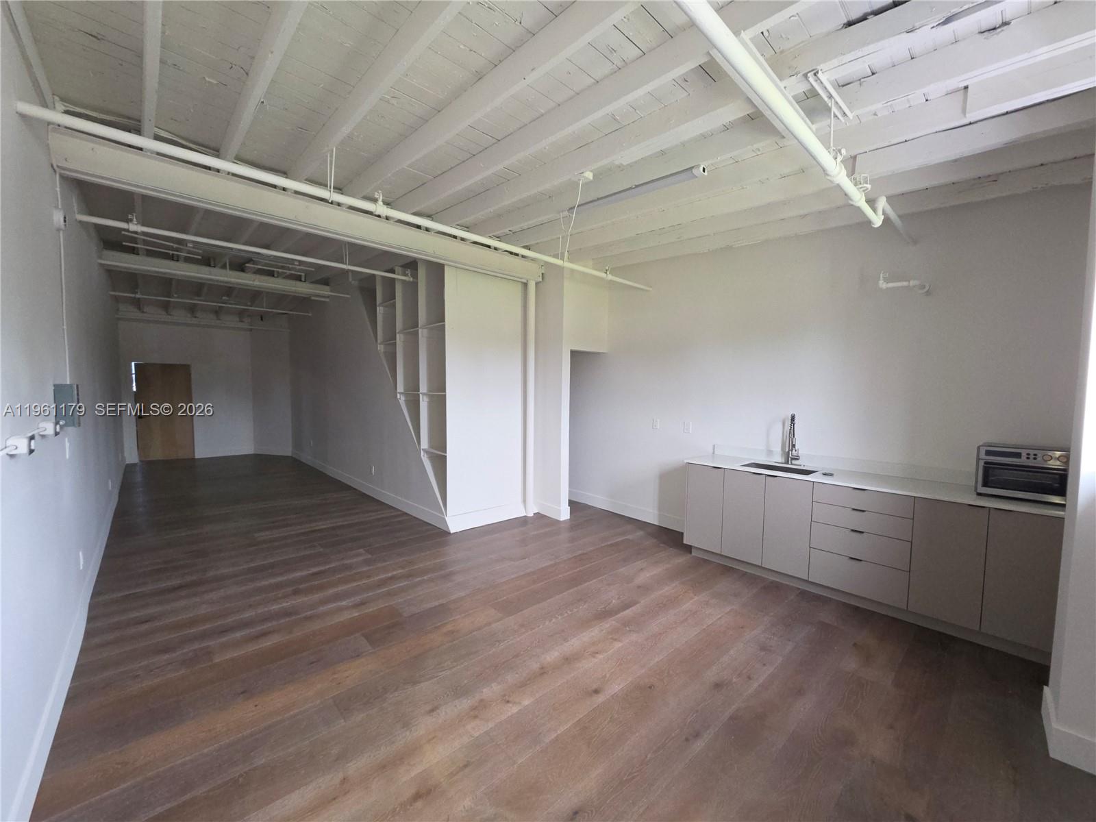 An open-concept studio space features white exposed ceiling beams, wood flooring, and a kitchenette — 164 NW 20th St # 202, Miami FL 33127, MIAMI, FL