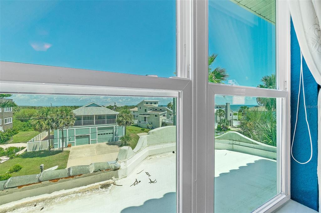 A view through a window showing a flat roof, neighboring houses, and the ocean — 54 OCEAN ST, PALM COAST, FL