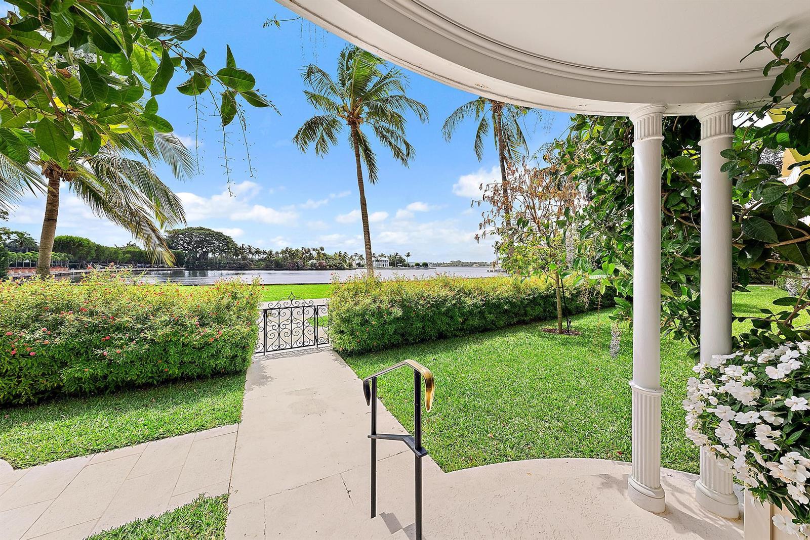A paved walkway leads through a garden toward a waterfront view with palm trees — 425 Worth Avenue # 2f, Palm Beach FL 33480, PALM BEACH, FL