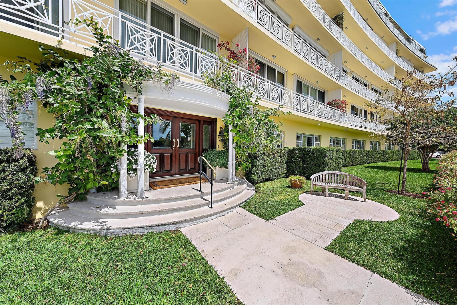 A yellow multi-story building features a covered entrance with double doors and a garden bench — 425 Worth Avenue # 2f, Palm Beach FL 33480, PALM BEACH, FL