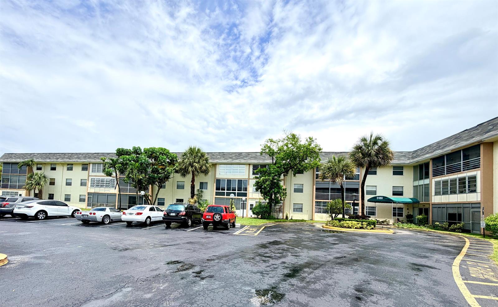 A multi-story apartment building with a parking lot in the foreground under a cloudy sky — 5180 E Sabal Palm Boulevard # 228, Tamarac FL 33319, TAMARAC, FL