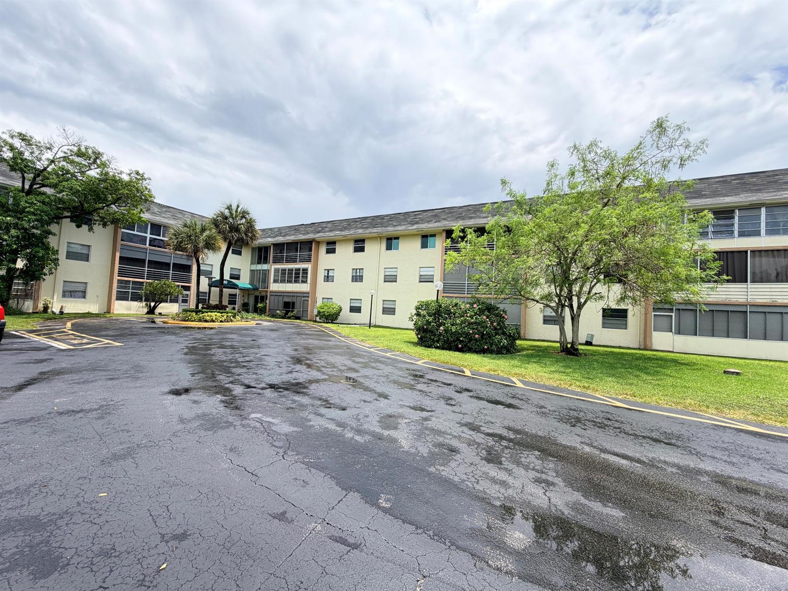 A multi-story apartment building with a parking lot and trees under a cloudy sky — 5180 E Sabal Palm Boulevard # 228, Tamarac FL 33319, TAMARAC, FL